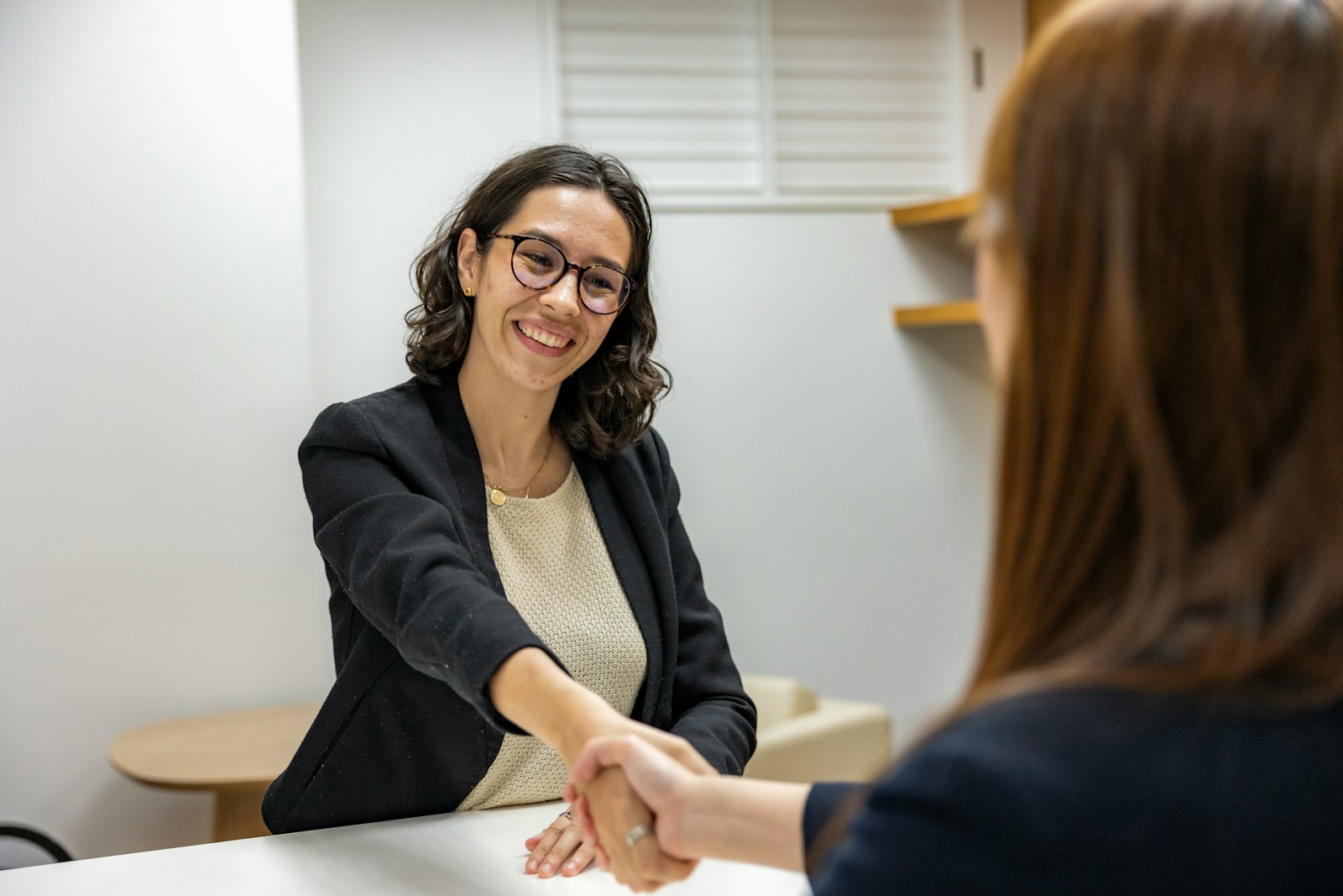 a woman shaking hands with another woman sitting at a table